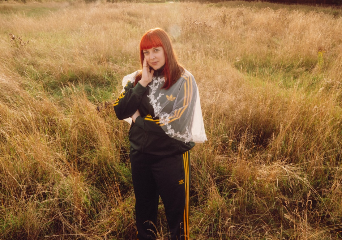 Producer and DJ Echo Juliet with red hair posed in dried grass field for The Unsigned Guide Spotlight July 2026 feature